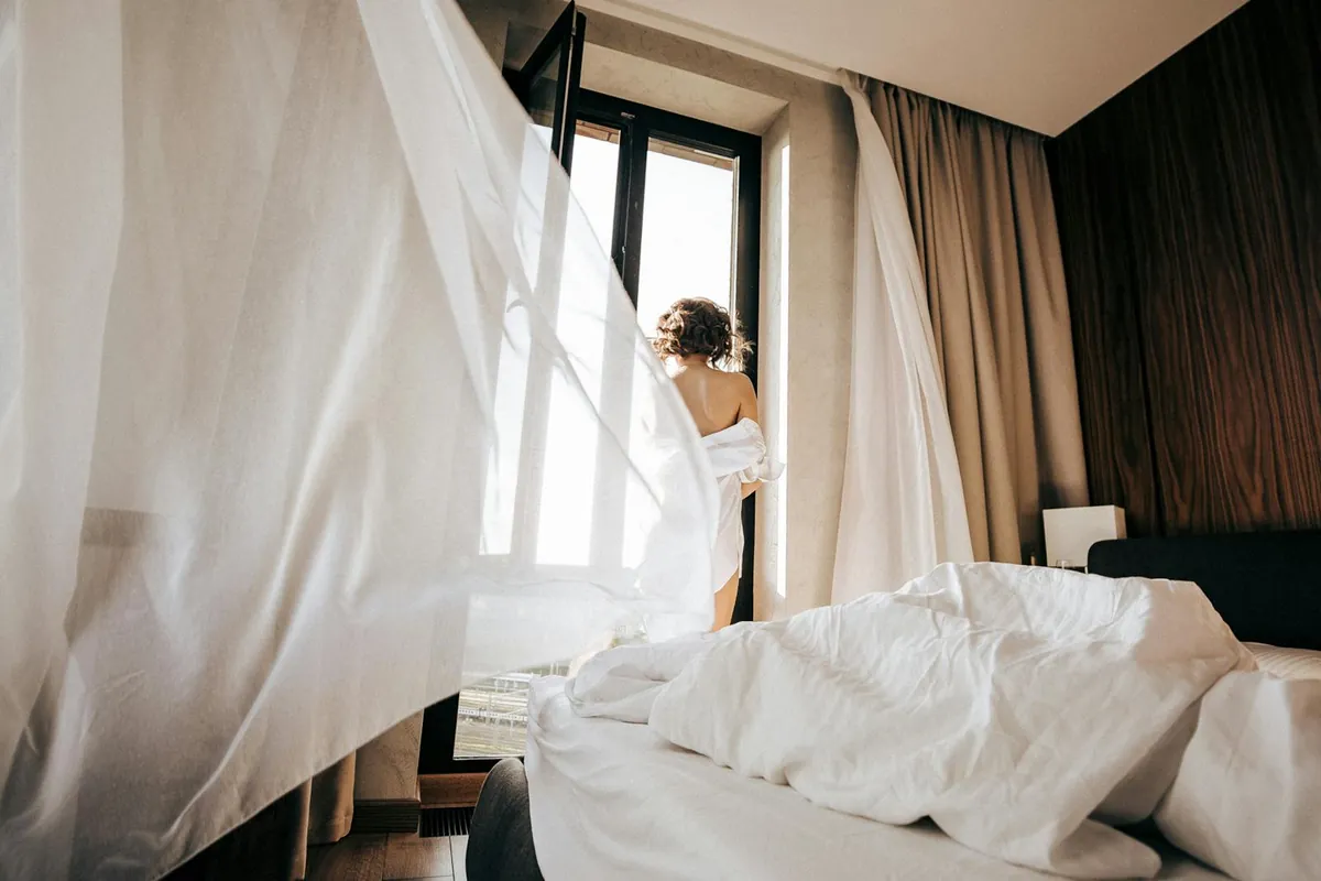 person opening curtains morning sunlight London window